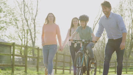 family on summer walk with pet bulldog in countryside with father teaching son to ride bike