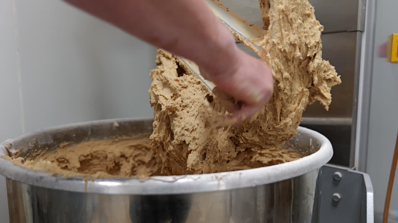 Nærbillede af hænder, der fjerner dejrester fra en stor industrimixer