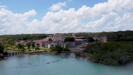 An-abandoned-colonial-town-in-mexico,-surrounded-by-lush-greenery-and-clear-waters,-under-a-cloudy-sky,-aerial-view