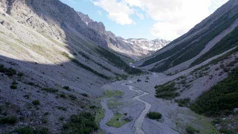 imágenes aéreas de drones rodando lentamente hacia la izquierda a través de un espectacular valle glacial rodeado de montañas empinadas y pinos con parches de nieve y un río alpino en suiza