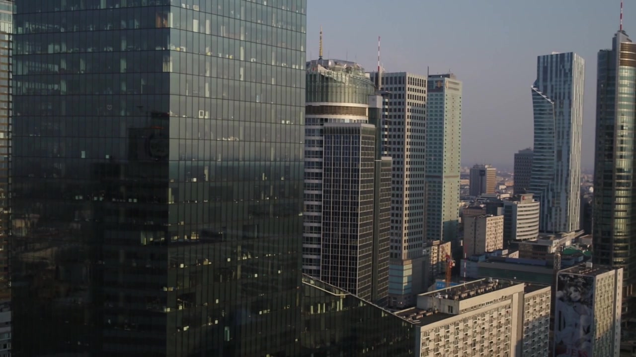 Vista aérea con dron que muestra modernos rascacielos de cristal y torres corporativas en el centro de Varsovia. La densa arquitectura urbana crea un impresionante paisaje urbano bajo un cielo despejado.