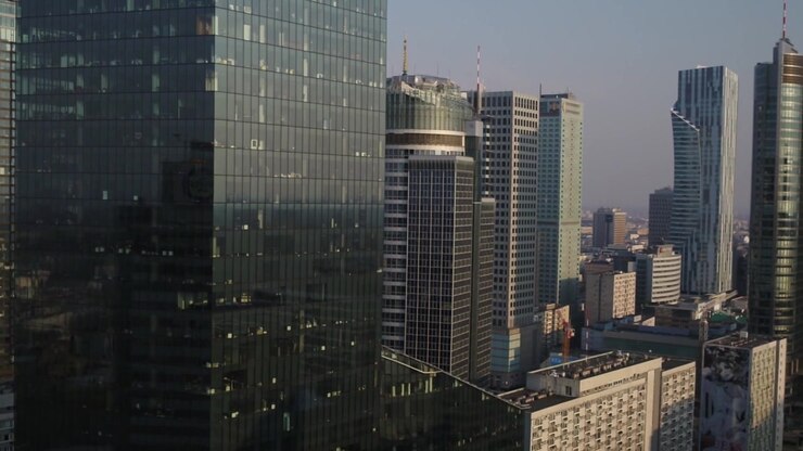 Vista aérea de drone mostrando arranha-céus modernos de vidro e torres corporativas no centro de Varsóvia. A arquitetura urbana densa cria uma paisagem urbana impressionante sob um céu limpo.