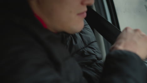 close up of road traveler putting on car seat belt while sitting beside fogged window wearing winter jacket focusing on hand movement safety preparation during commute