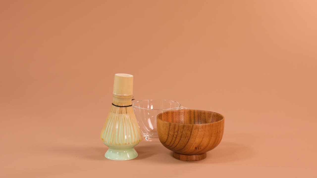 Hånden heller vann fra glassmugge i treskål ved siden av bambusvisp, myk studiobelysning