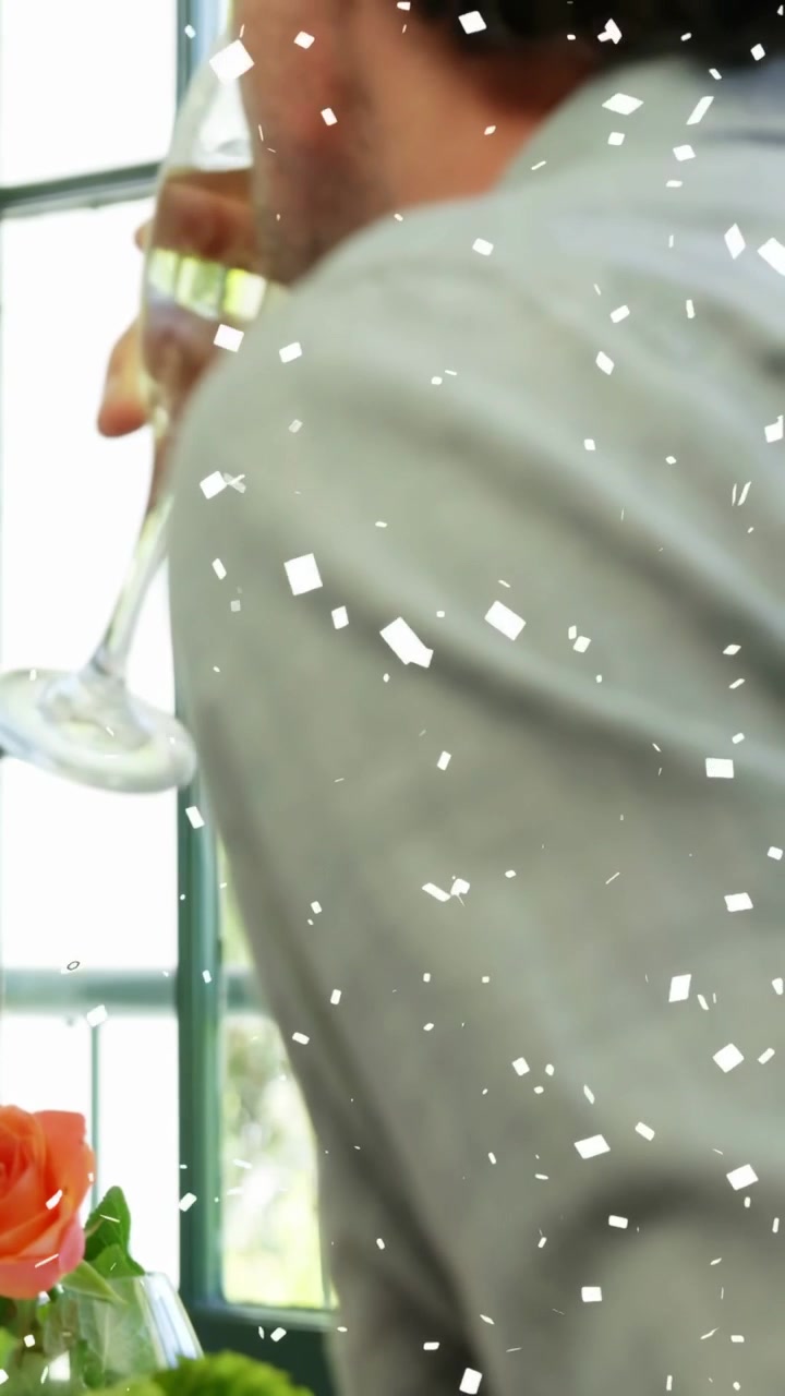 Couple dining, woman reaching across table leading man sipping champagne, confetti overlay floating