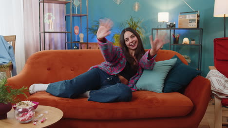 caucasian woman smiling friendly at camera waving hands gesturing hello hi greeting at home on sofa