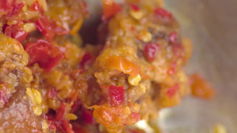 Colorful-traditional-authentic-sambal,-oily-chili-paste,-stirred-and-mixed-together-in-cooked-mentai-chicken-with-silver-spoon-in-metal-bowl,-extreme-close-up-static