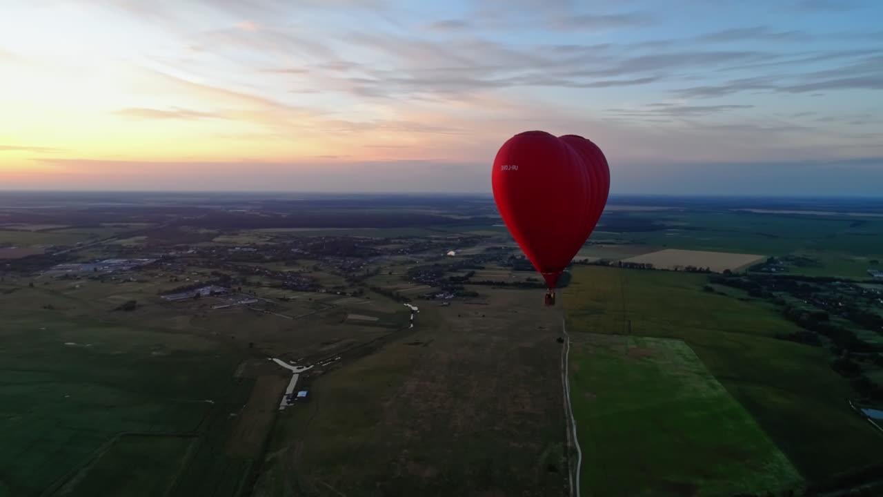 Red aerostat against the setting sun. Hot air balloon flying in the sky over the field in the countryside. Hot air balloon in the form of a heart. Aerial view.