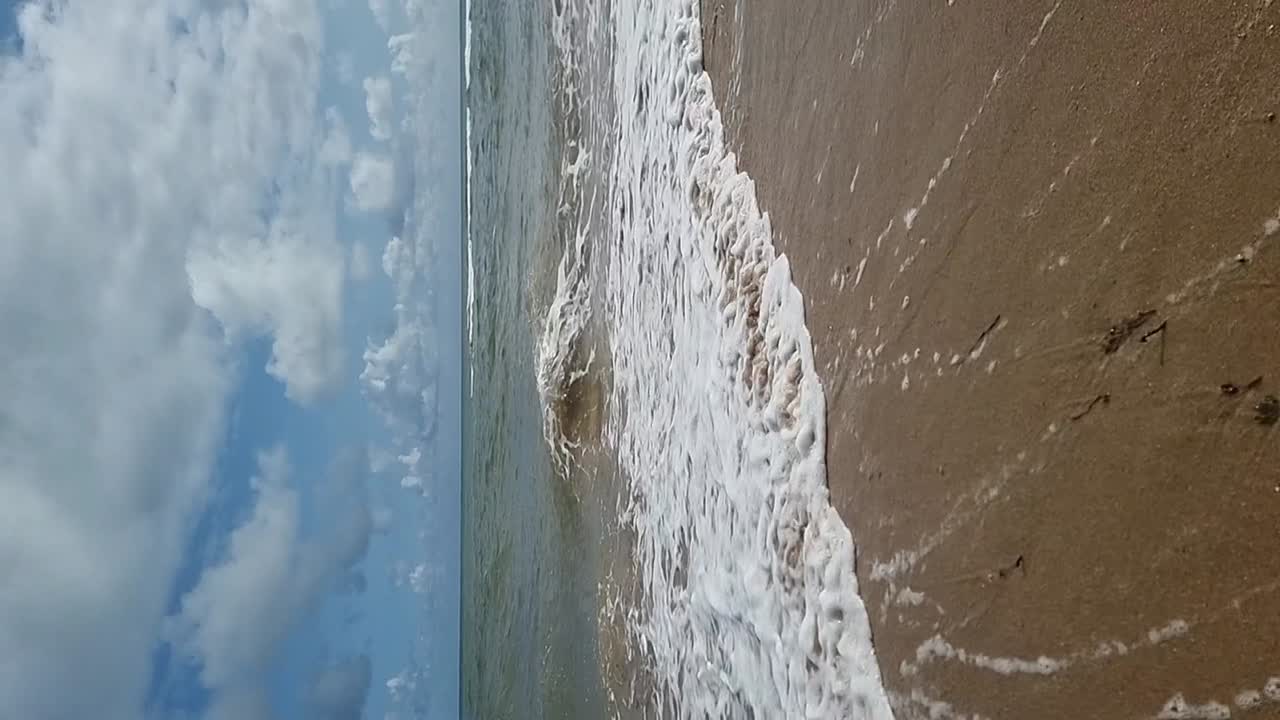 VERTICALE Onde oceaniche tropicali al rallentatore che scorrono su una spiaggia di sabbia dorata sotto un cielo blu nuvoloso