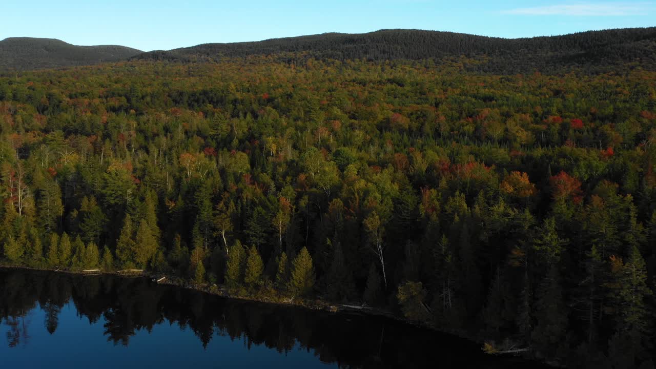 un dron aéreo disparó sobre el borde de un lago de montaña con coloridos árboles de otoño a lo largo de la costa cuando termina el verano y la temporada cambia para caer en maine