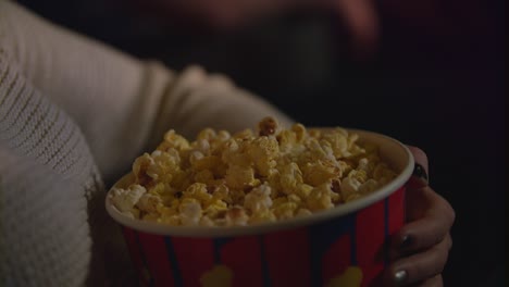 mano femenina tomando palomitas de maíz de un recipiente de papel. comiendo palomitas de maíz en el cine
