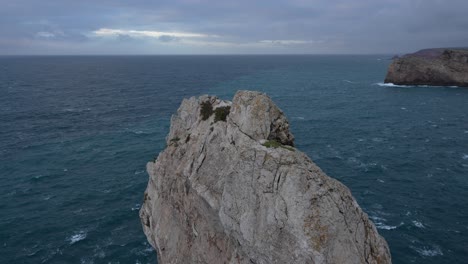 roca gris que sobresale del agua azul del océano atlántico en el extremo suroeste de portugal, durante una puesta de sol nublada