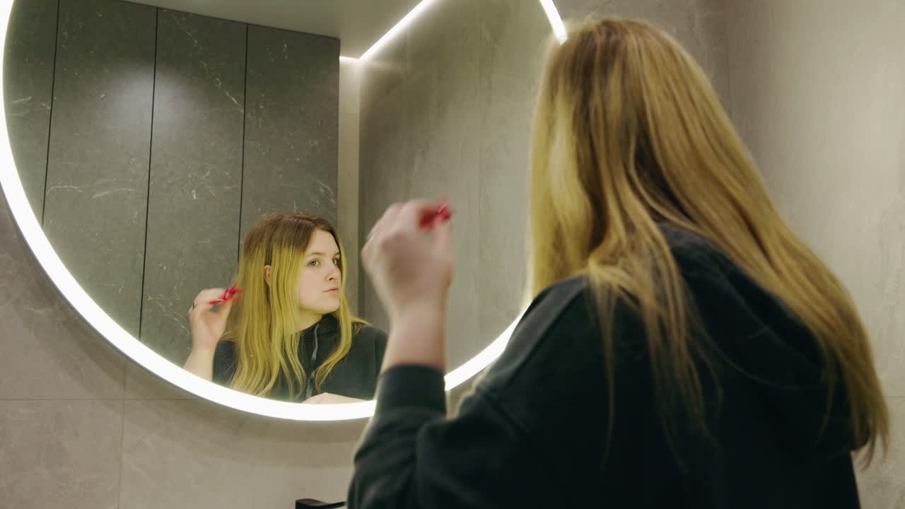 Woman styling her hair in front of a bathroom mirror
