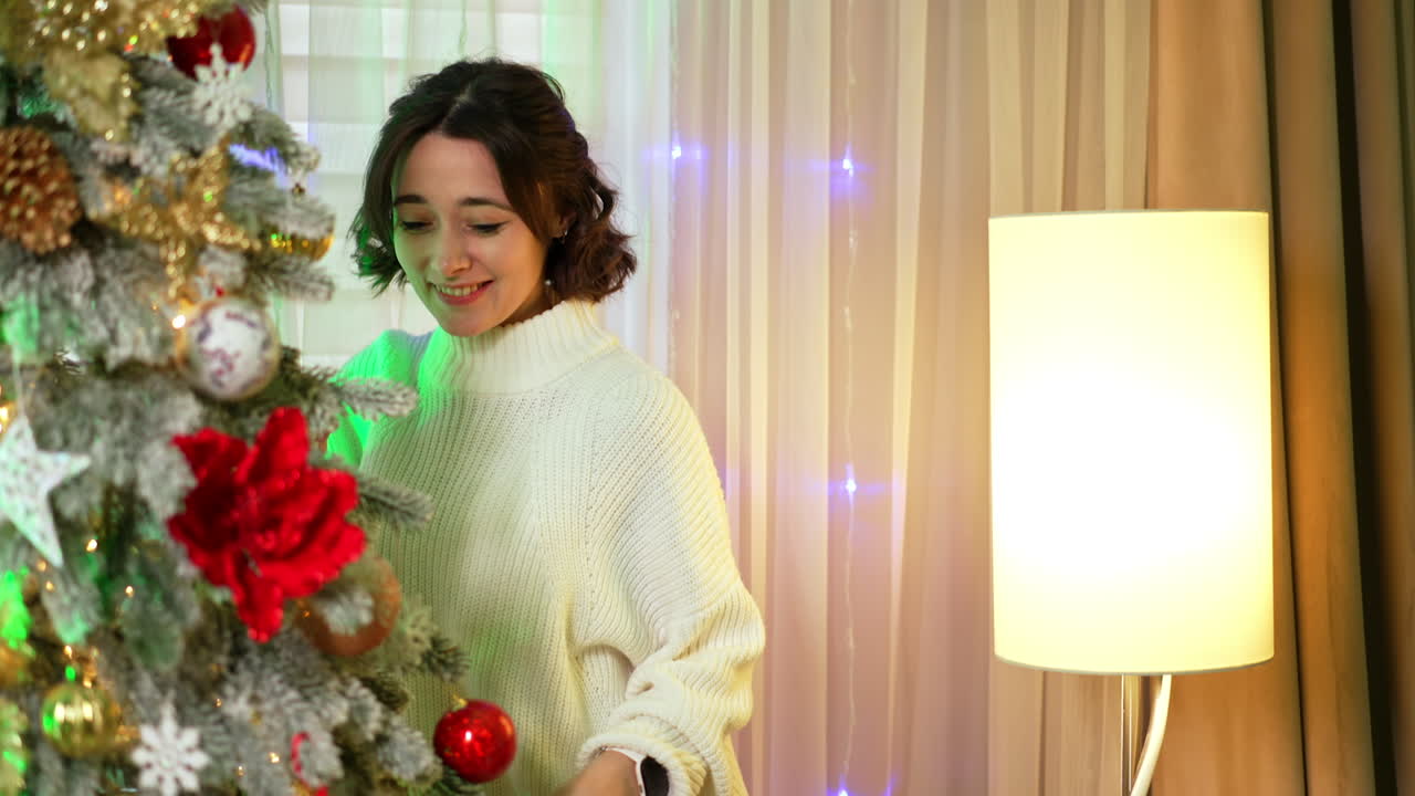 Joyful Caucasian brunette decorates a fir tree. Happy woman at home for Christmas. Close up.