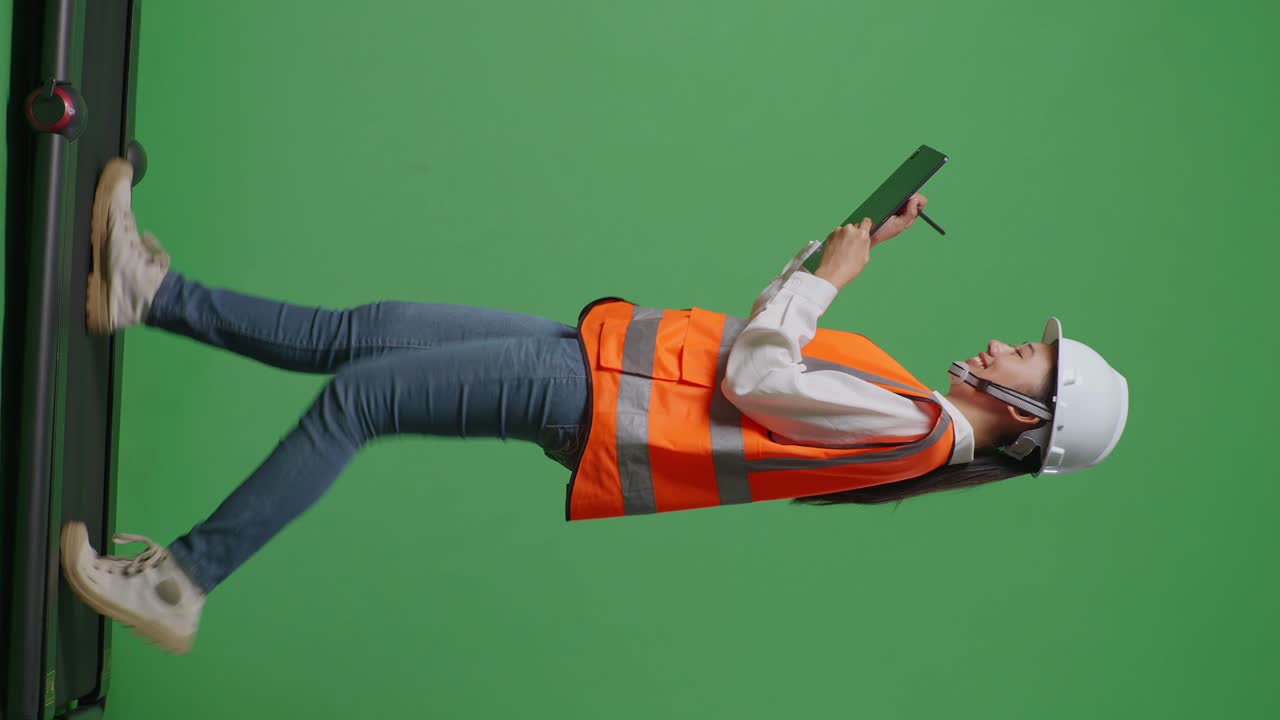 안전 헬을 입은 아시아 여성 엔지니어가 녹색 화면 배경 스튜디오에서 는 동안 태블릿에 메모를 취합니다.