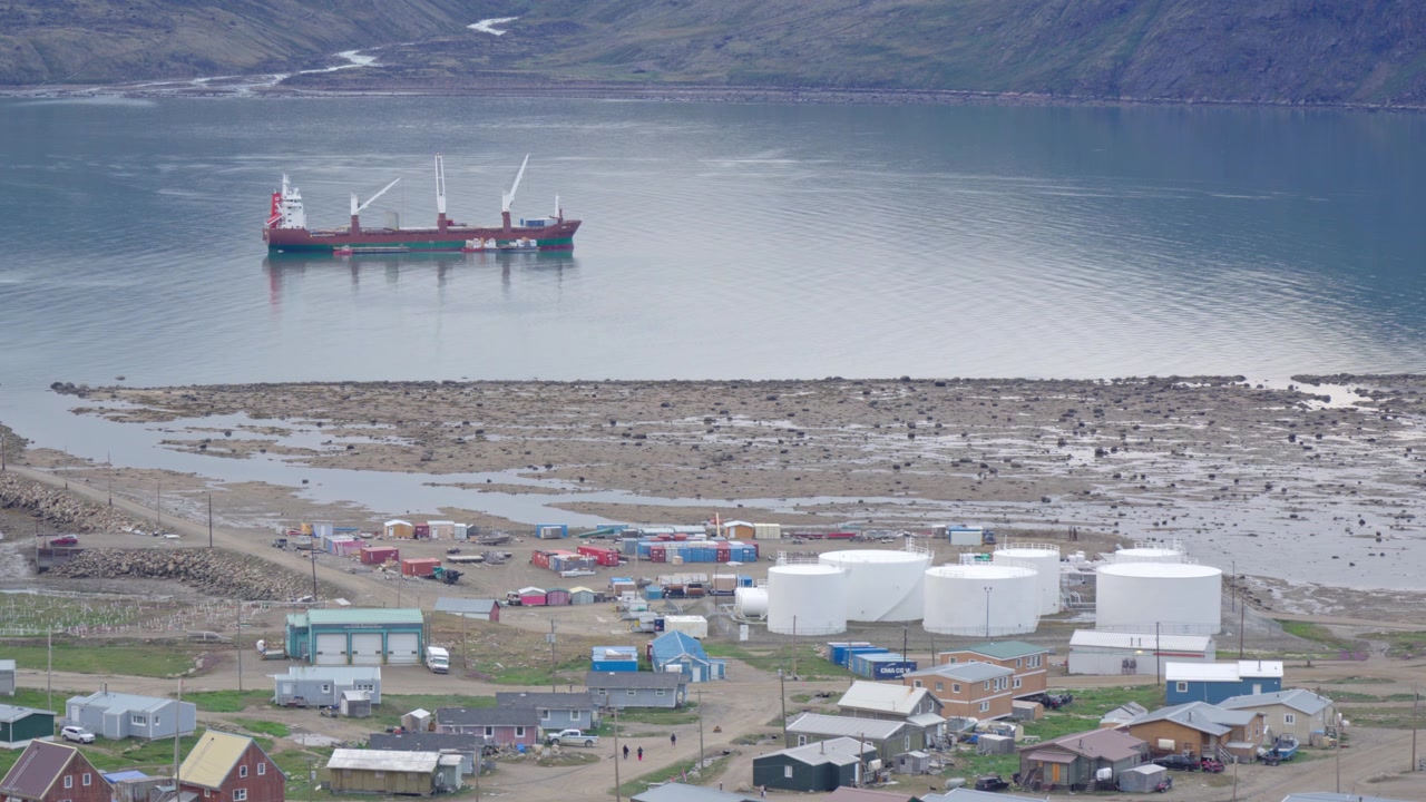 Mellomdistansebilde som fanger et sealift lasteskip ankret opp i Pangnirtungbukta, plassert utenfor kysten nær drivstofflagertanker på land og industrielle oppsamlingsområder