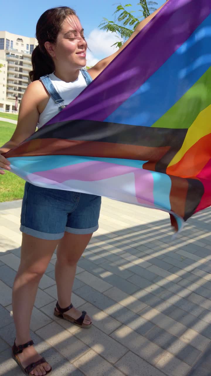 Young woman holding progress pride flag in the wind