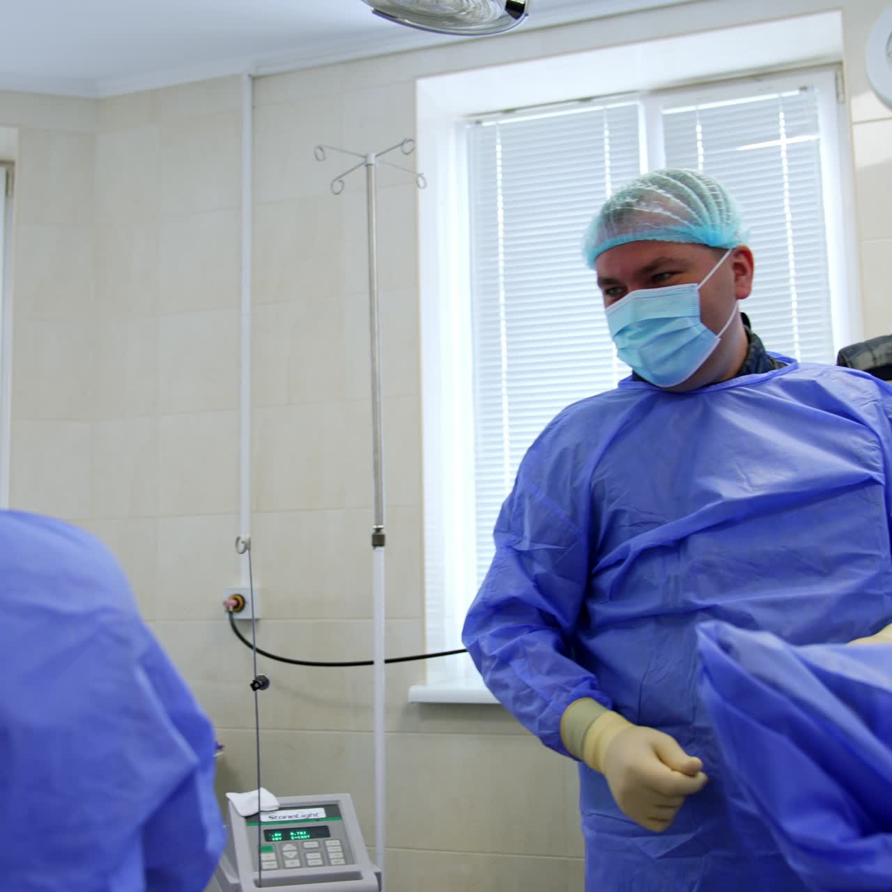 Male surgeon puts away the medical device. Doctor raises hands up rejoicing about the successful end of operation. Low angle view