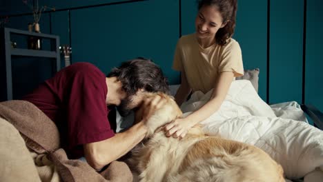 a brunette and a brunette are stroking a dog in bed against a turquoise wall. hanging out with your pets at home