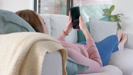 Entspannte-Kaukasische-Frau,-Die-Auf-Der-Couch-Liegt-Und-Ihr-Smartphone-Mit-Kopierraum-In-Zeitlupe-Benutzt