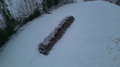 circular drone view over a pile of wood stacked in a snow covered meadow