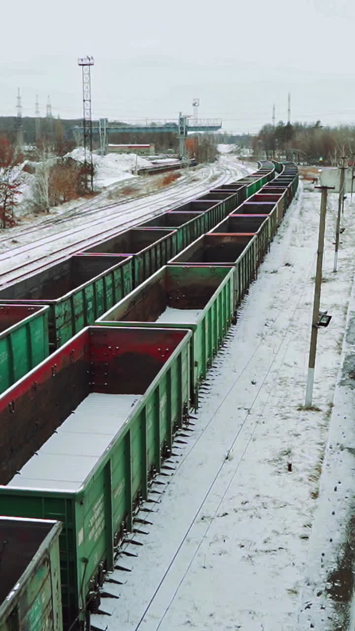 Empty shipping containers are located at an abandoned railway station in the countryside against the background of snow and forest. Aerial view. Vertical video