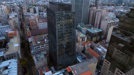 un rascacielos moderno en medio del paisaje urbano al anochecer, las luces comienzan a iluminar la escena, el entorno urbano, vista aérea