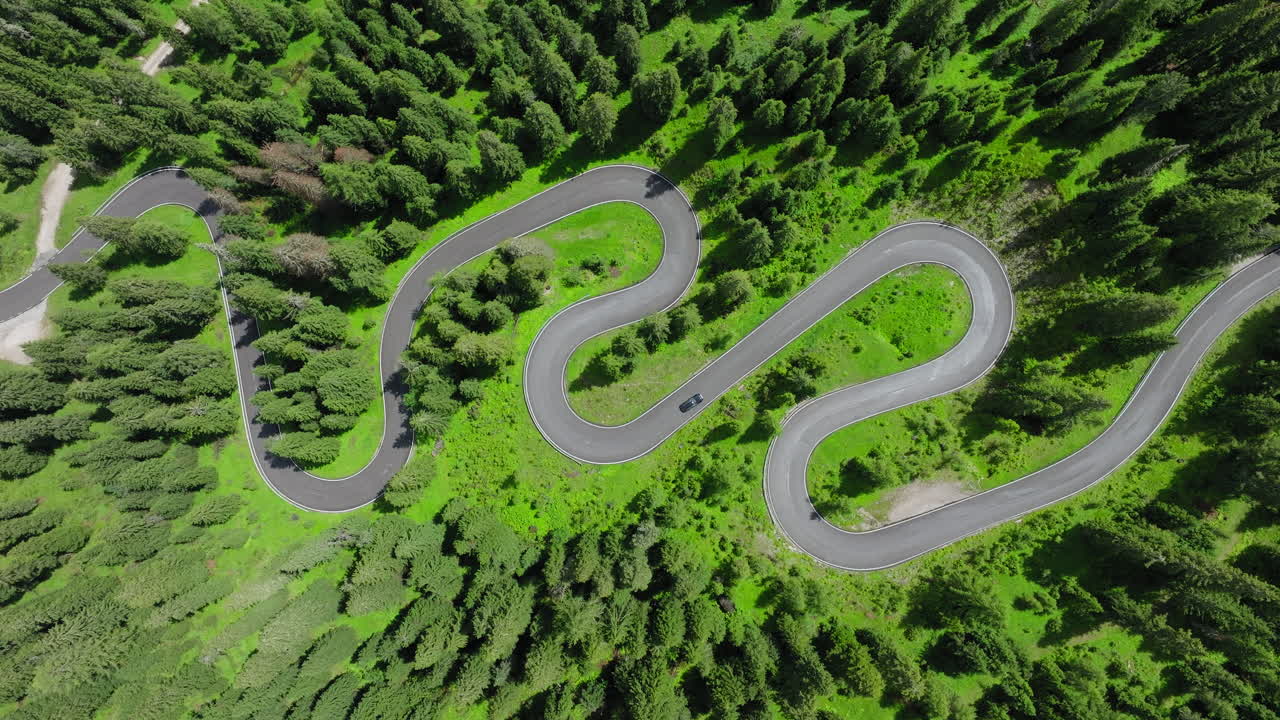 Aerial top down of serpentine road near Giau Pass weaving through forested Dolomites terrain