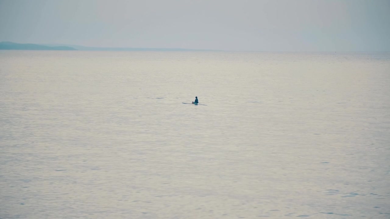 Persona che pagaia su oceano calmo con orizzonte nebbioso.