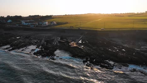 the drone is flying backwards and rising in height to show the beautiful rocky beach of malahide during a golden hour