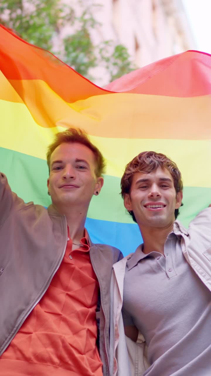 Happy Gay Couple Holding Rainbow Flag and Smiling Outdoors