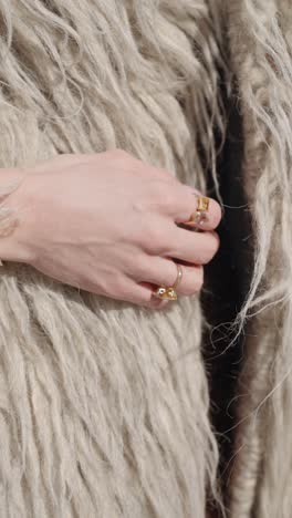 a close-up shot of a hand adorned with gold rings and bracelets, resting against a textured, shaggy beige fabric, showcasing elegant jewelry and a soft, natural aesthetic