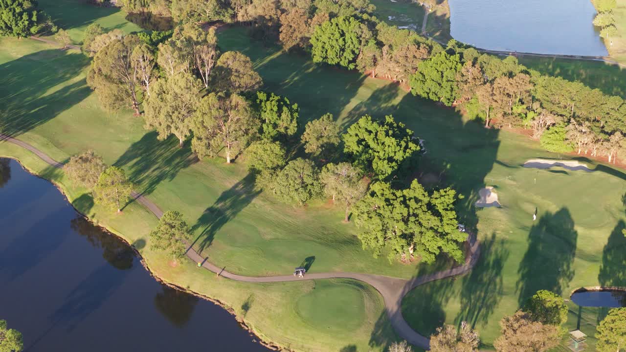 Drone footage captures a lush golf course with water hazards and trees during golden sunset hour in Gold Coast, Australia