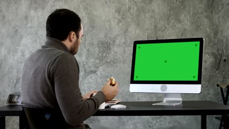 young man choking while eating and watching something on the computer in the office. green screen mock-up display