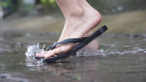 low angle of a flipflops feet stomping playing on water puddle on the raining day,  flooding water on the street side, enjoying splashing dirty water, jumping goofy around, tropical raining season