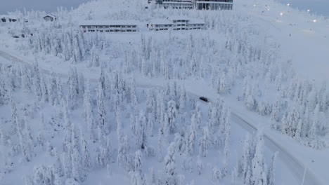 Aerial-view-following-a-car-driving-up-to-the-top-of-the-Iso-Syote-fell,-winter-in-Finland