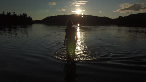 wide sunset shot of a woman walking out of the water after a swim in black lake