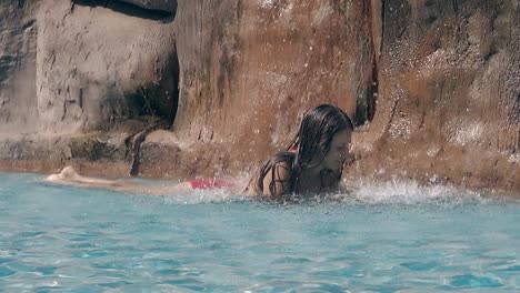 lady takes rest under falling waterfall drops in hotel pool