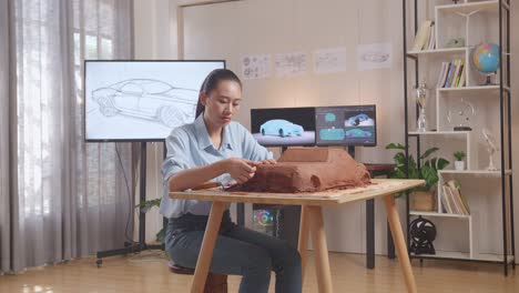 mujer asiática diseñadora de automóviles trabaja en la escultura de arcilla de automóviles usando sus manos para suavizar la superficie y crear detalles en el diseño en el estudio