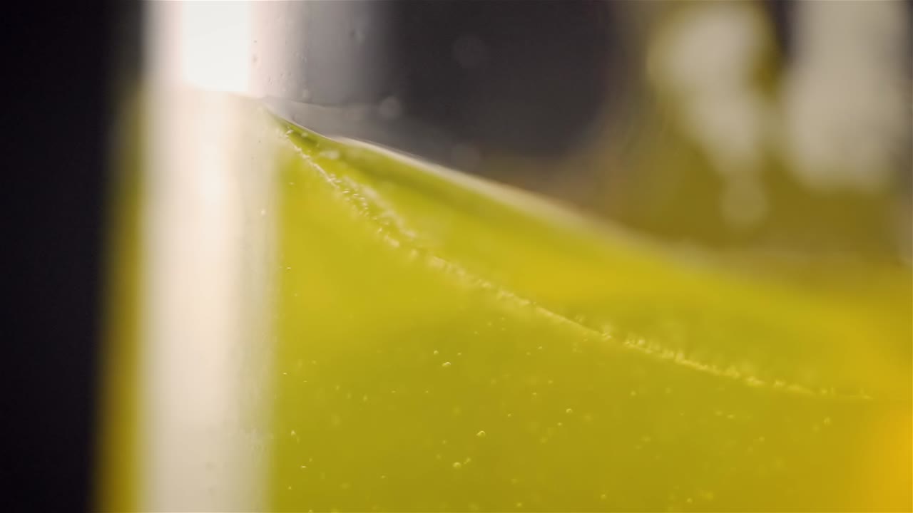 Sideview shallow depth of field of yellow drink liquid spinning around in glass in slow motion