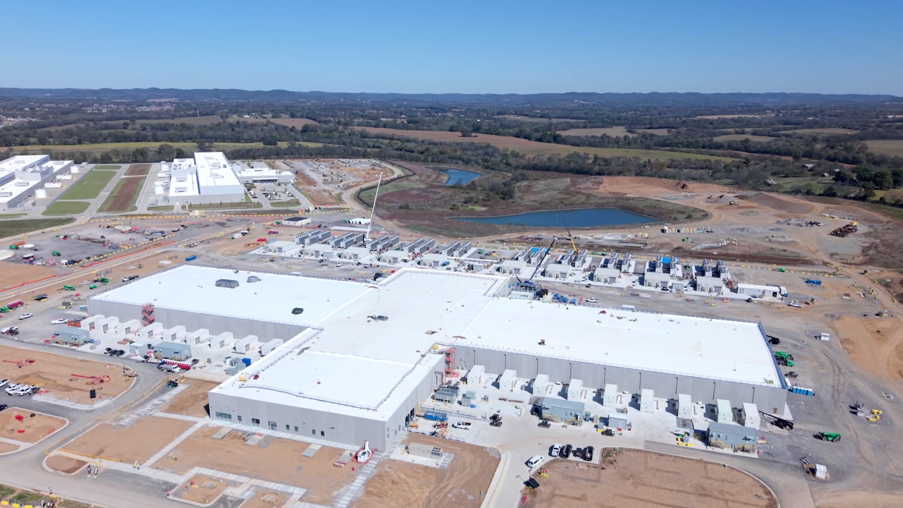 Aerial view approaching large data center campus with industrial buildings and surrounding landscape in daylight