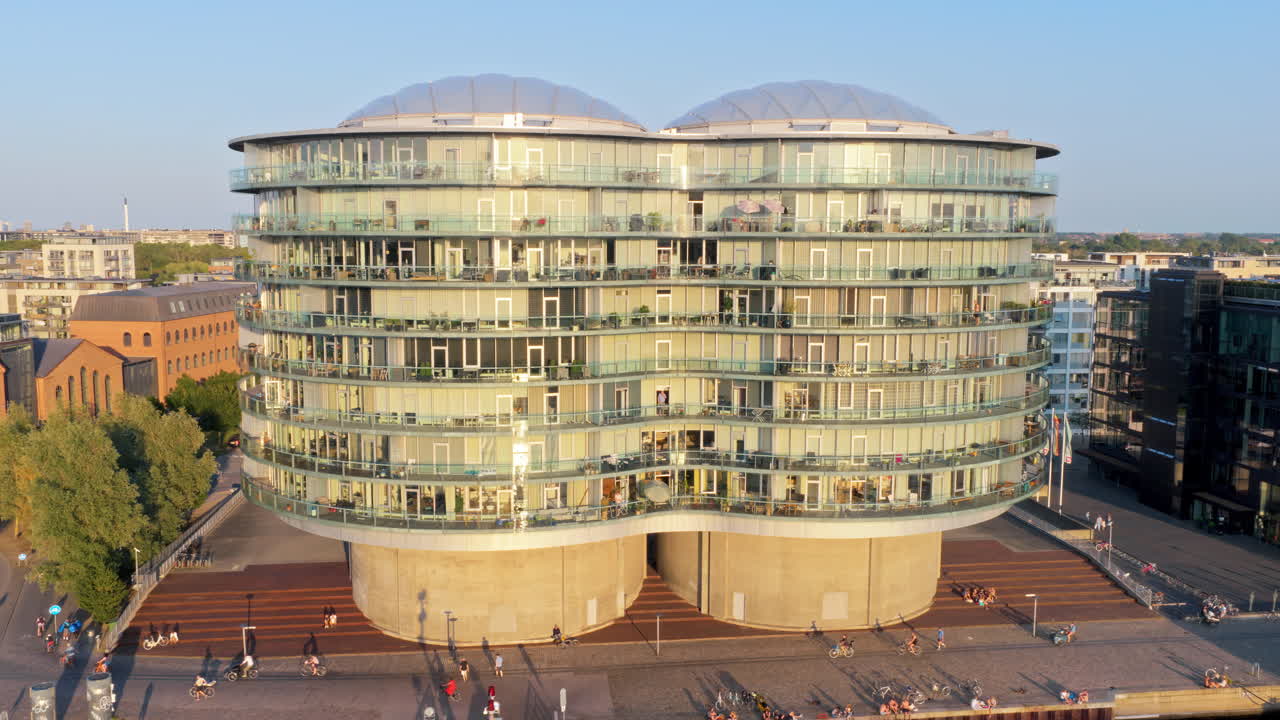 Copenhagen, Denmark - August 6, 2025: Aerial drone view of the Gemini Residence, futuristic round glass building built on old silos, standing at the waterfront of Islands Brygge
