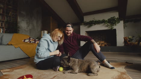 couple playing with her bulldog dog with a tennis ball on the floor in living room 3