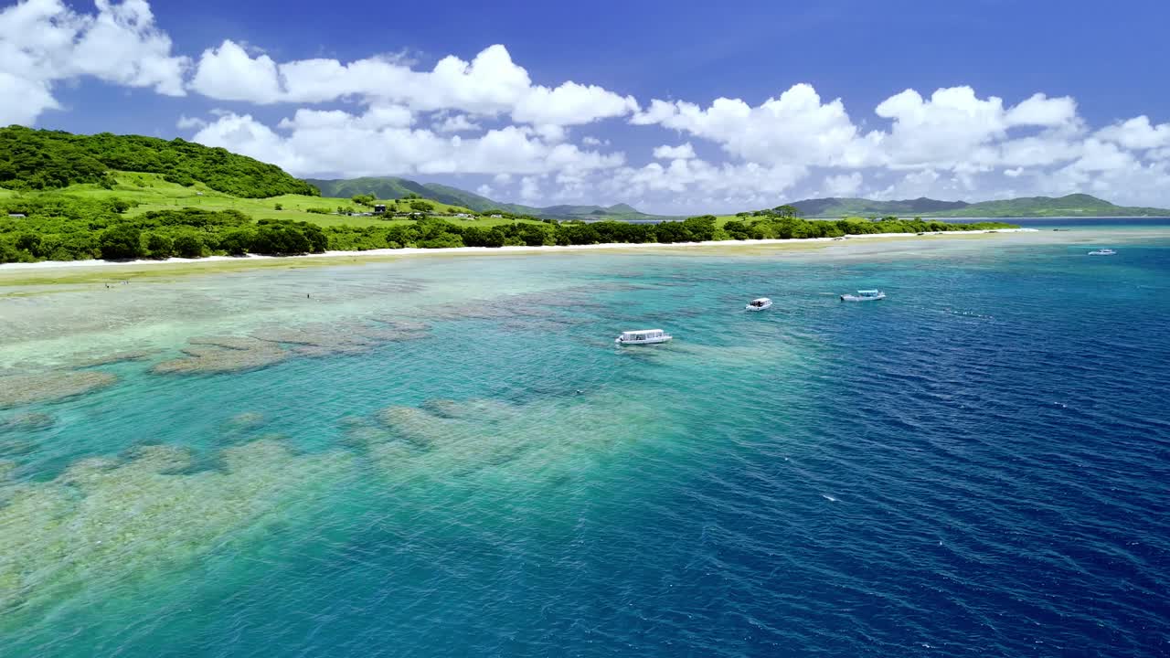 Una ripresa panoramica con drone cattura barche con fondo di vetro che galleggiano su vivaci barriere coralline nelle acque turchesi della Baia di Kabira, Ishigaki, sotto un pittoresco cielo nuvoloso