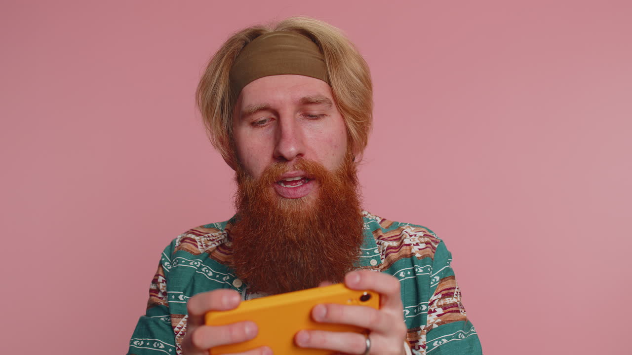 걱정하는 히피 우승자 스마트폰 가 ⁇  앱에서 드라이브 레이싱 또는 슈팅 비디오 게임을 하는 남자