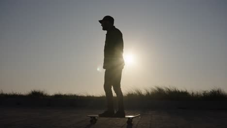 Scenic-sunset-tracking-shot-of-skateboarder-silhouette-riding-down-pavement