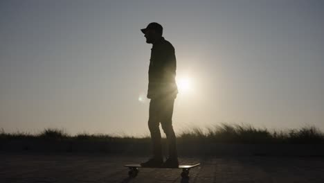 Toma-De-Seguimiento-Escénica-De-La-Puesta-De-Sol-De-La-Silueta-De-Un-Patinador-Bajando-Por-El-Pavimento