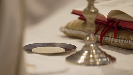 communion wafer on a silver paten, with a chalice and prayer book nearby