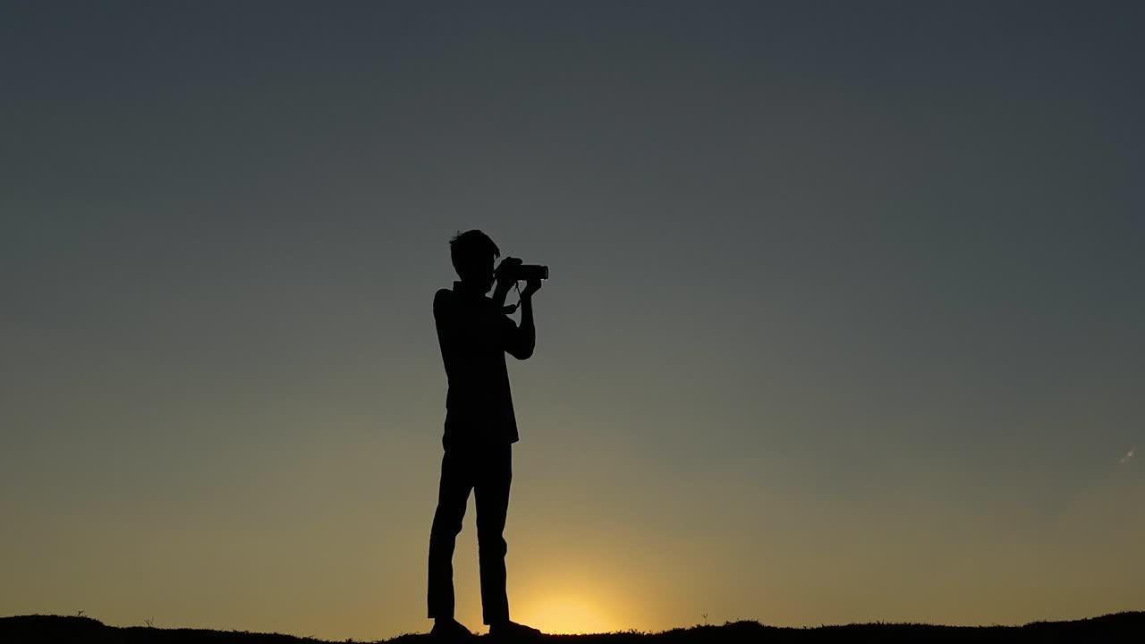 Silhueta de fotógrafo com câmera, tirando fotos no céu ao pôr do sol, em close-up.