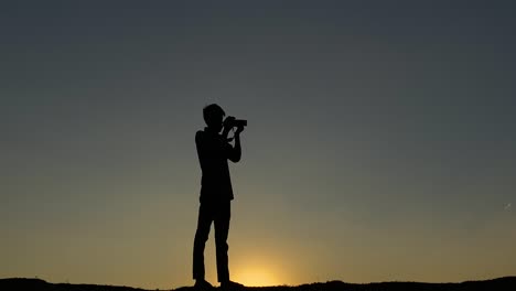 silhouette of photograher with camera taking pictures at sunset sky, zoom in